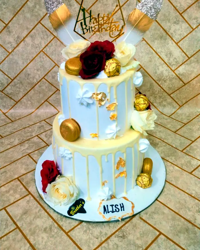 A two-tier drip cake decorated with red and white roses and a gold Happy Birthday topper