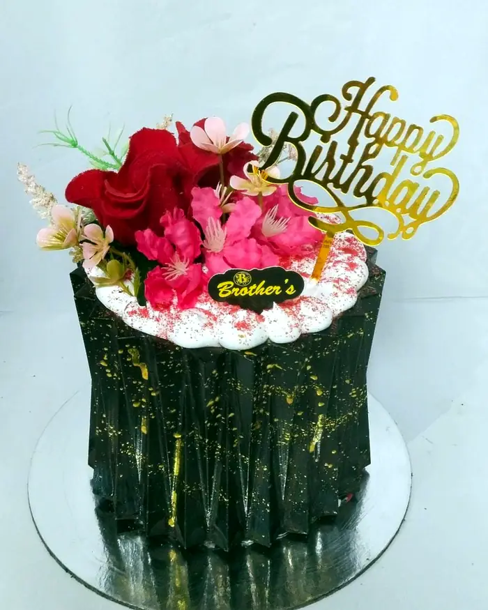 A fluted dark chocolate cake topped with fresh flowers and a gold Brother's Bakers badge