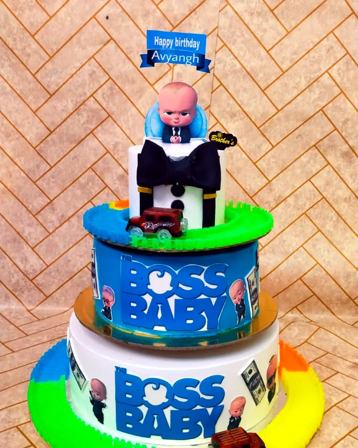 A three-tier cartoon-themed birthday cake with a toy car track around the base