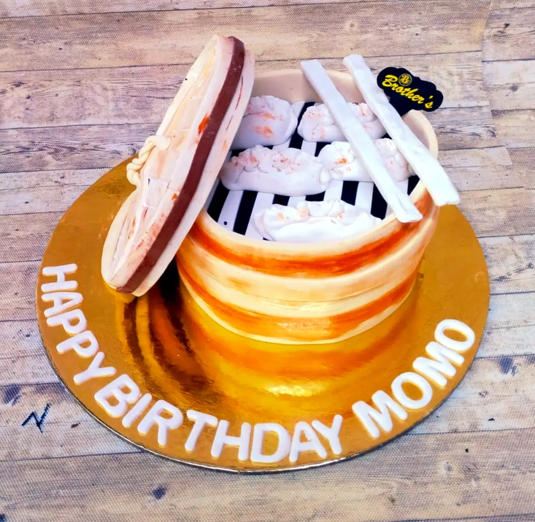 A birthday cake iced to look like a bamboo momo steamer, lid propped open, fondant momos and chopsticks inside